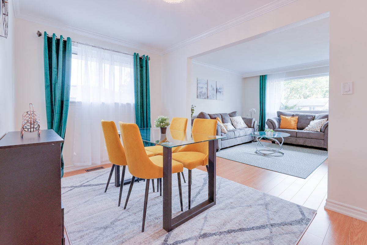 Dining room with a glass table, four mustard chairs and a bright adjoining living room
